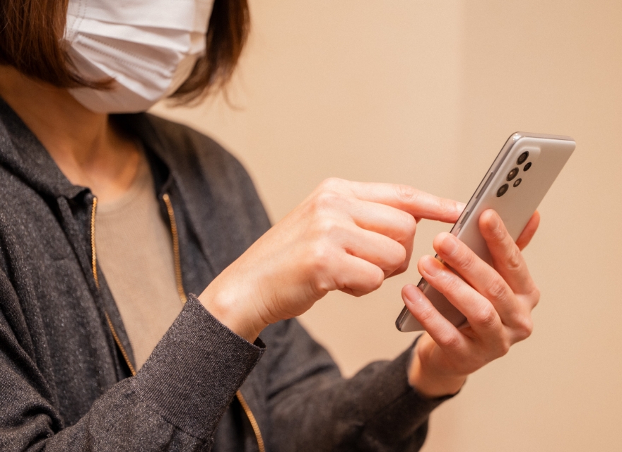 マスクをつけた女性が携帯で予約をする様子